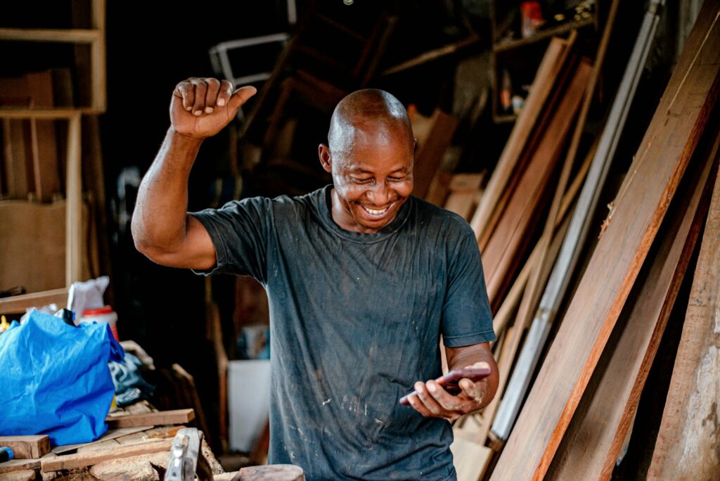 A carpenter celebrating a message on his phone in his workshop