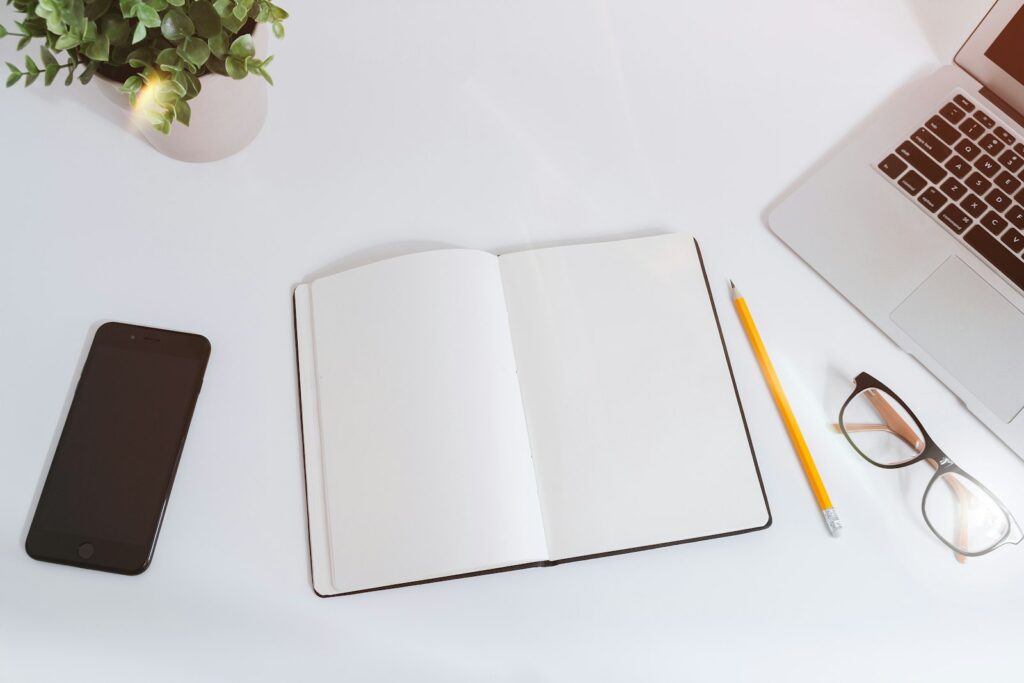 A notebook, phone and laptop laid out on a white desk
